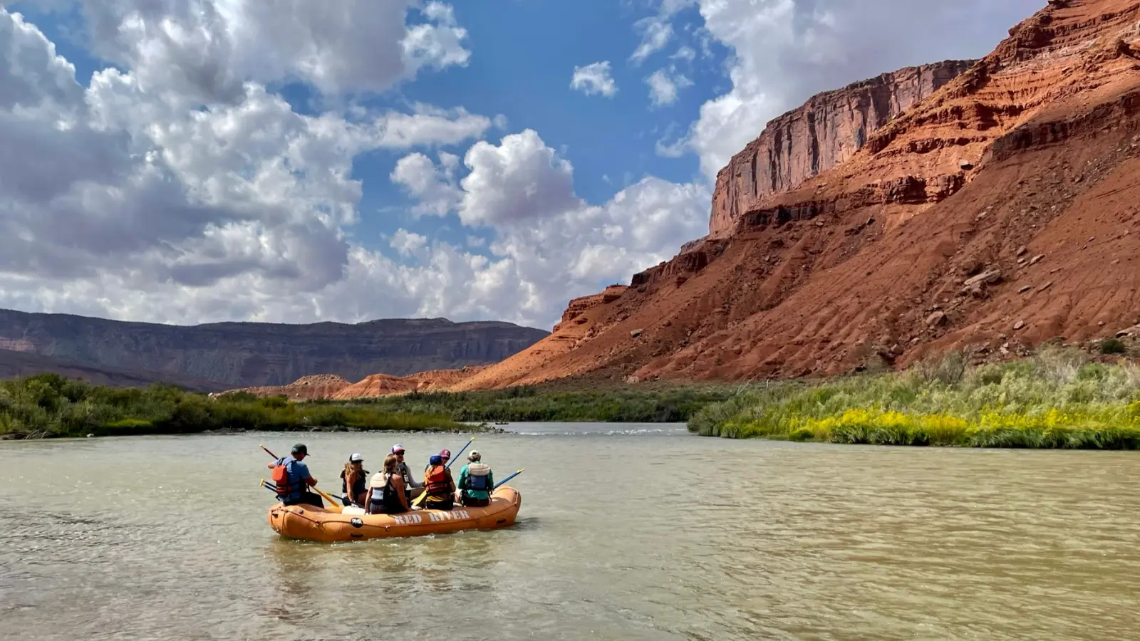 An orange boat floats down a scenic river canyon
