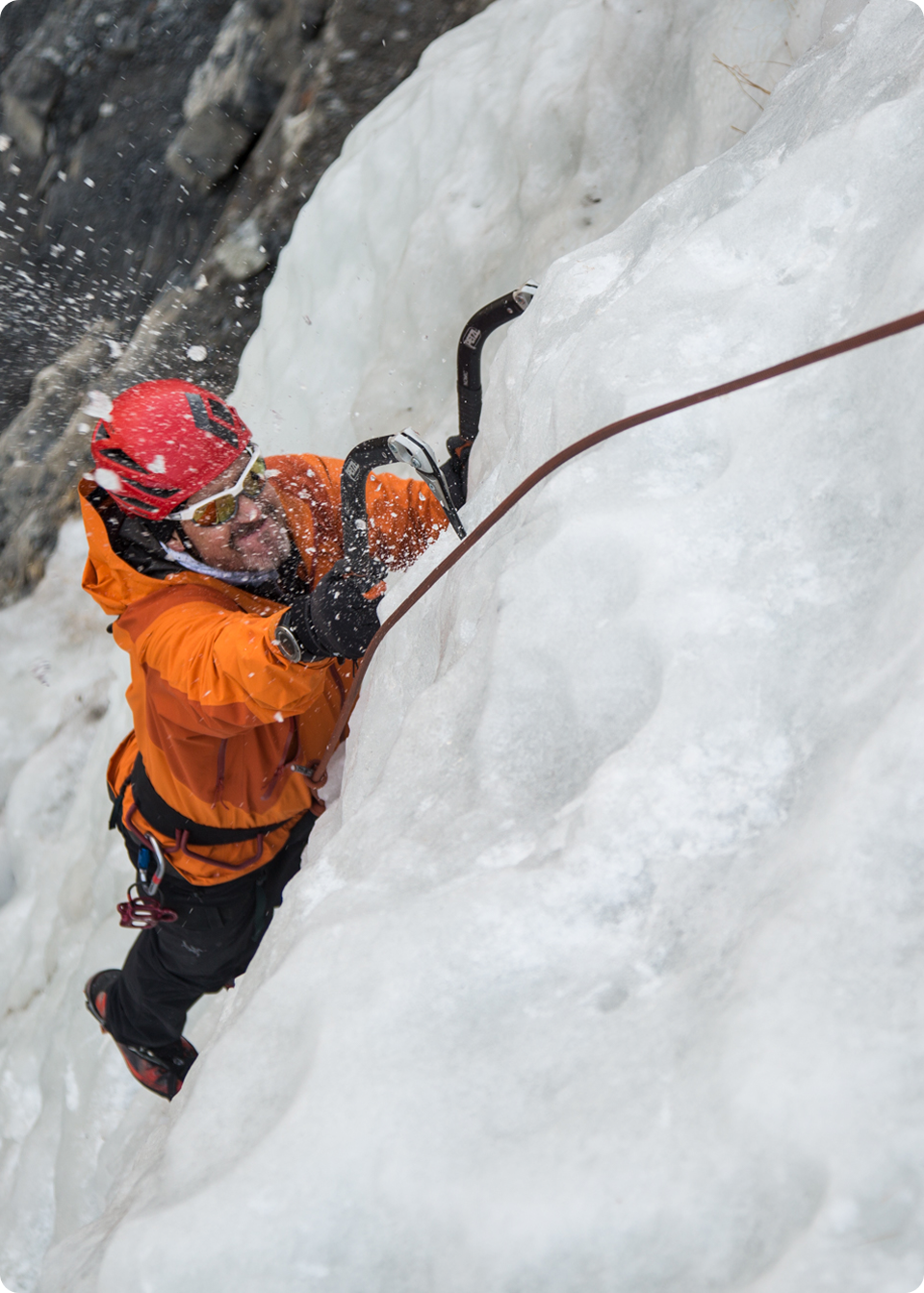 A man ice climbing in an orange jacket