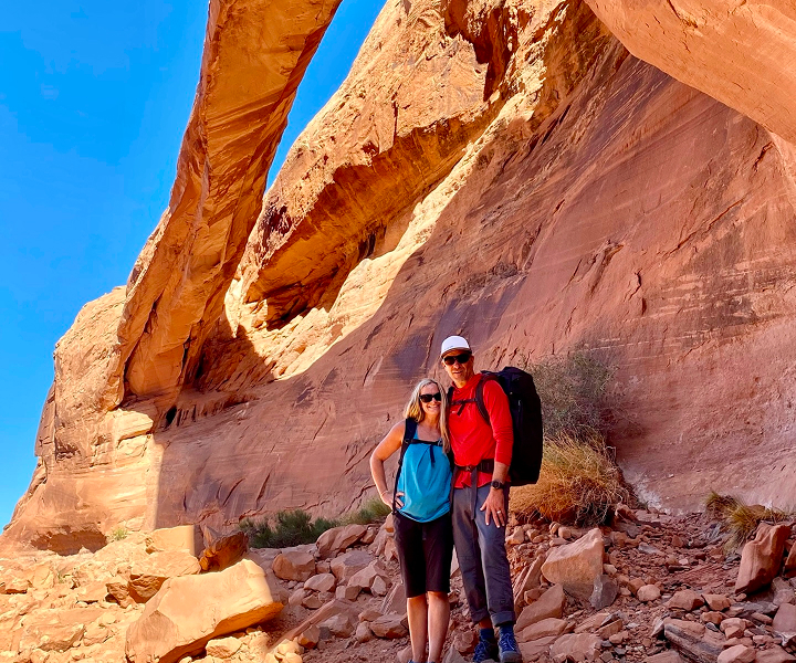 two people smiling under a natural arch in moab