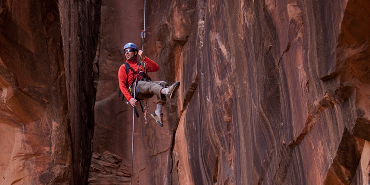 A man in red rappels down the morning glory arch in moab