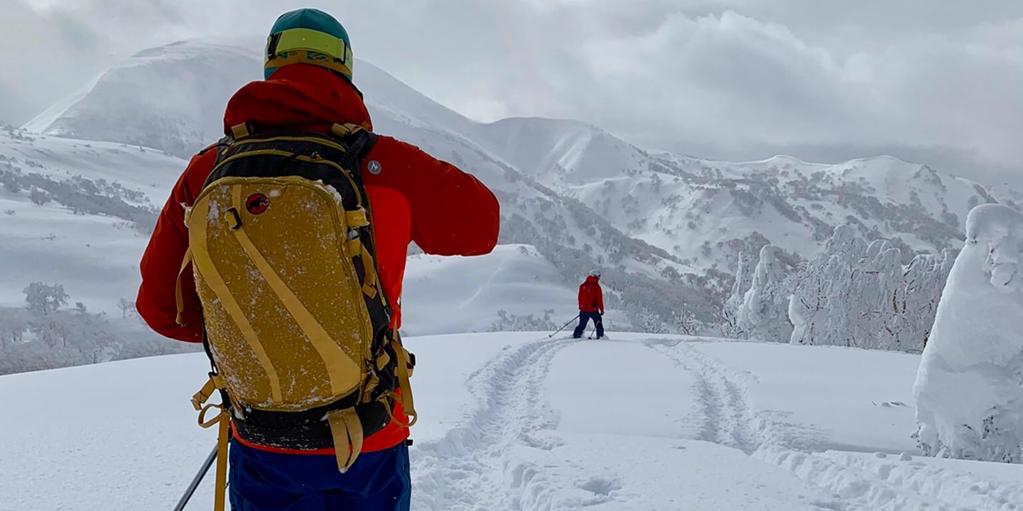 Two people backcountry skiing on a grey day