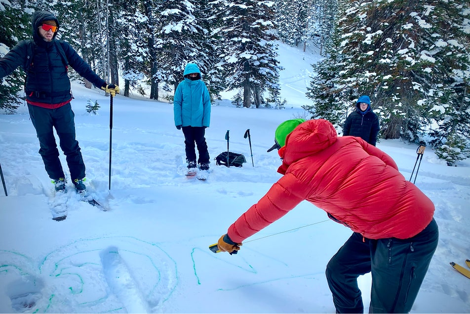 A person teaches an Avalanche Courses outside in the snow to three others