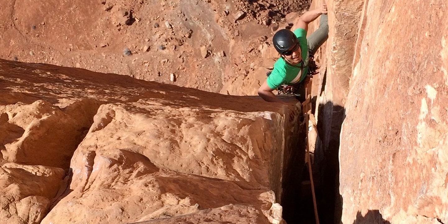 A man in a green shirt clilmbing castleton tower in moab
