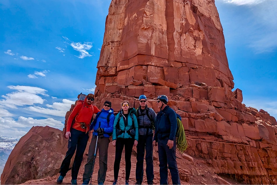 A group of people stand in front of the popular climbing destination castleton tower in Moab