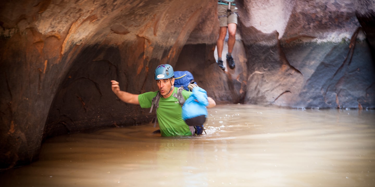 A man on a canyoneering trip who is wading through water in a slot canyon