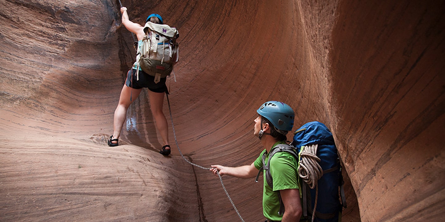 A man belays a woman while canyoneering