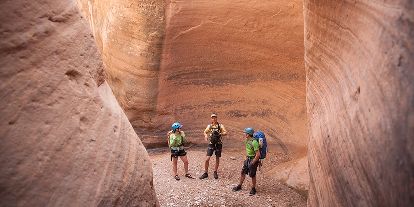 Three people stand in the middle of a tight slot canyon