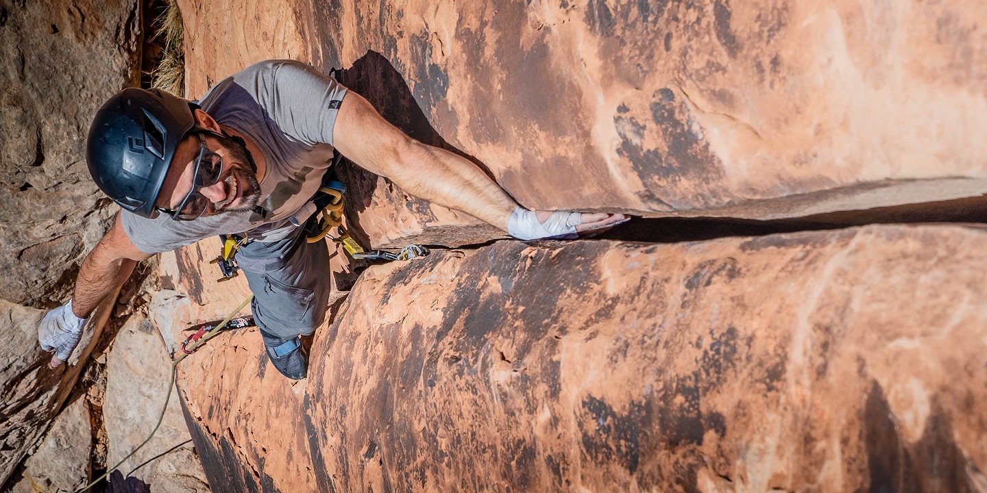 A person crack climbing pauses to put chalk on his hand
