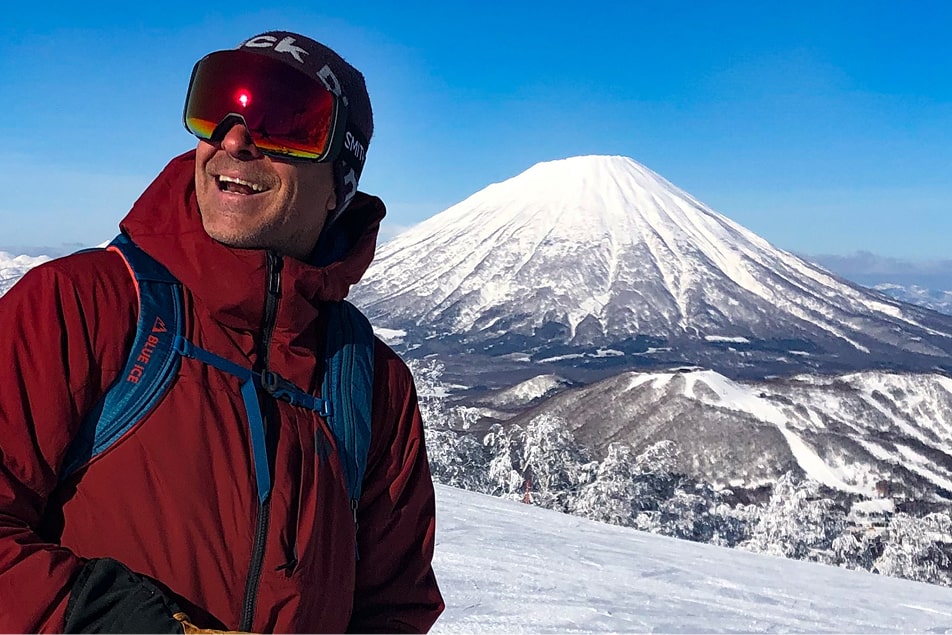 A man in ski gear smiles in front of a volcano in hokkaido