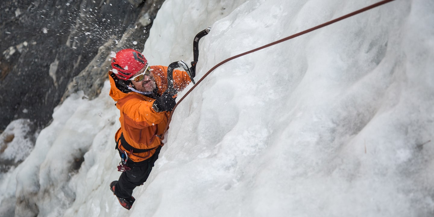 A man in an orange jacket is ice climbing