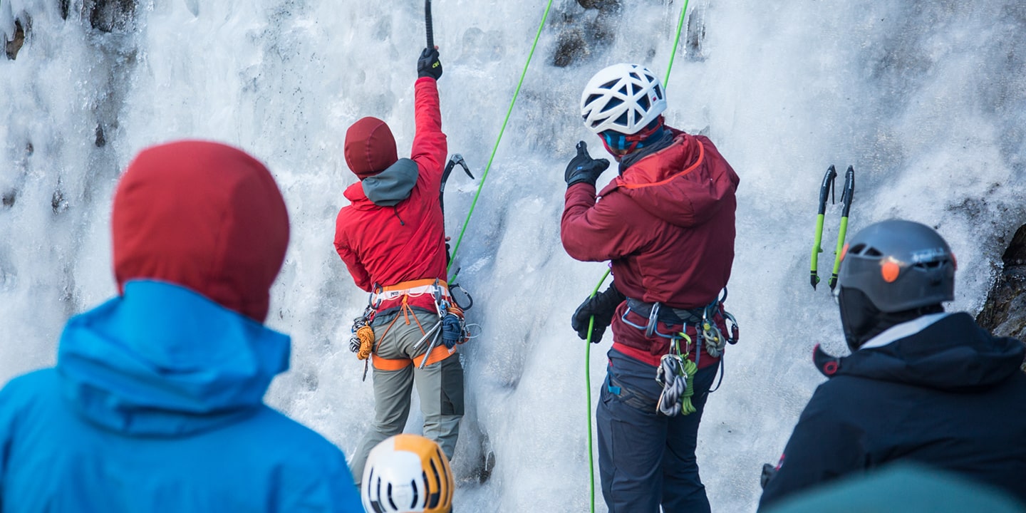 A man coaches others on ice climbing technique