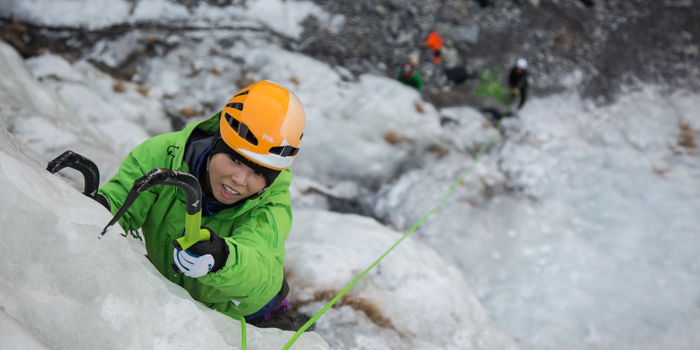 A woman in a green jacket places her ice axe as she ice climbings