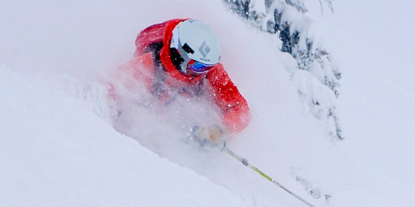 A man in a red jacket skiing in powder