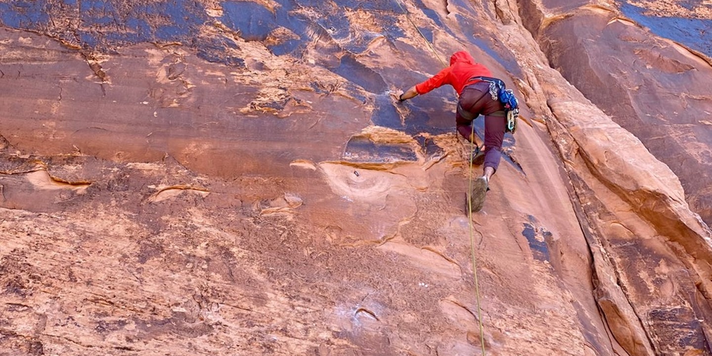 A man rock climbs in a red jacket