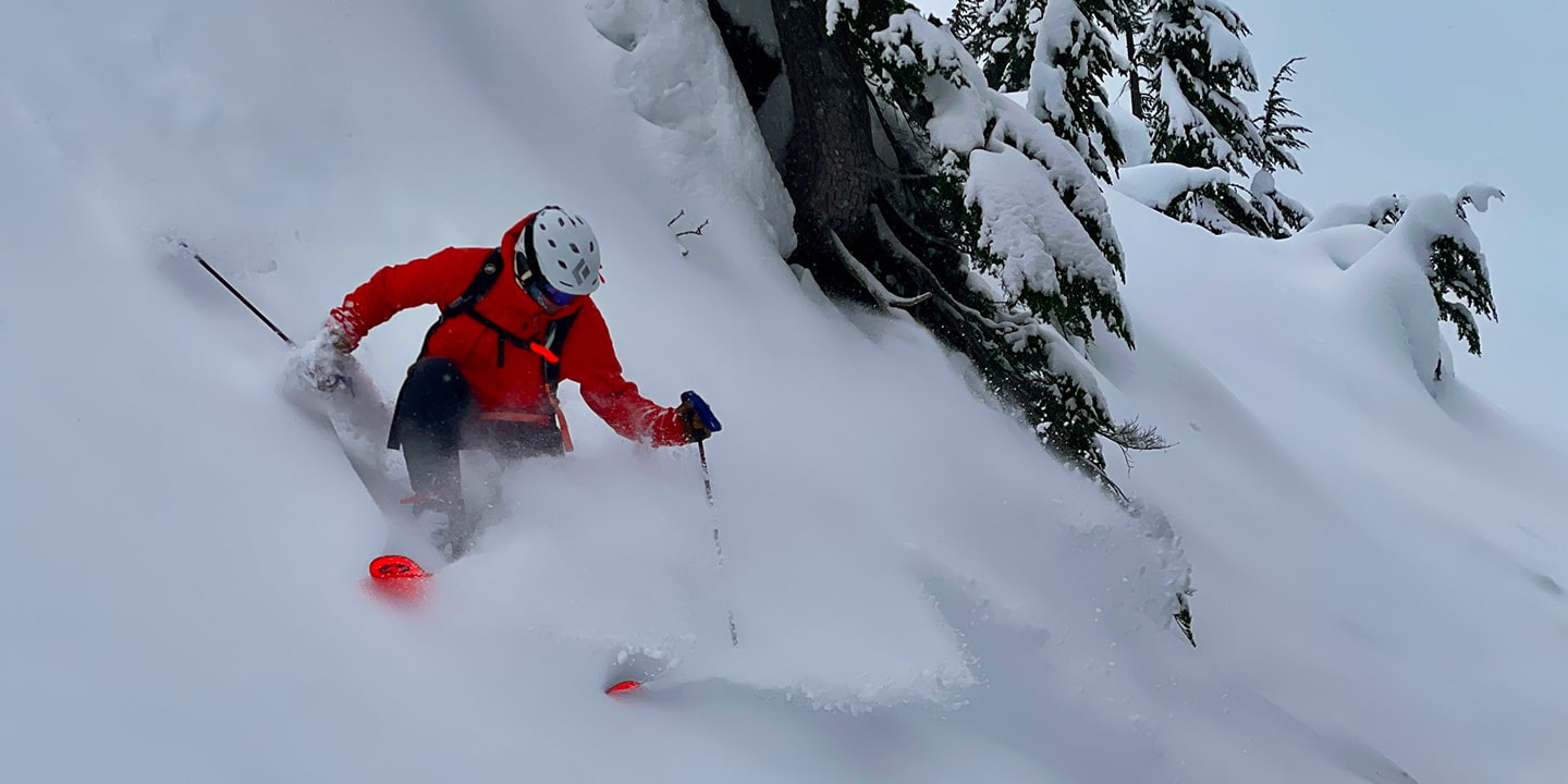 A man skis down a steep mountain in powder