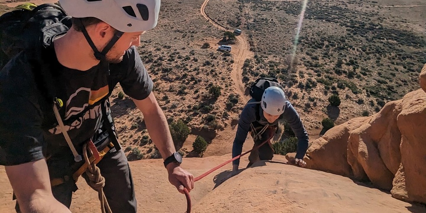 A guide helps a rock climbing up the last section of looking glass arch in moab
