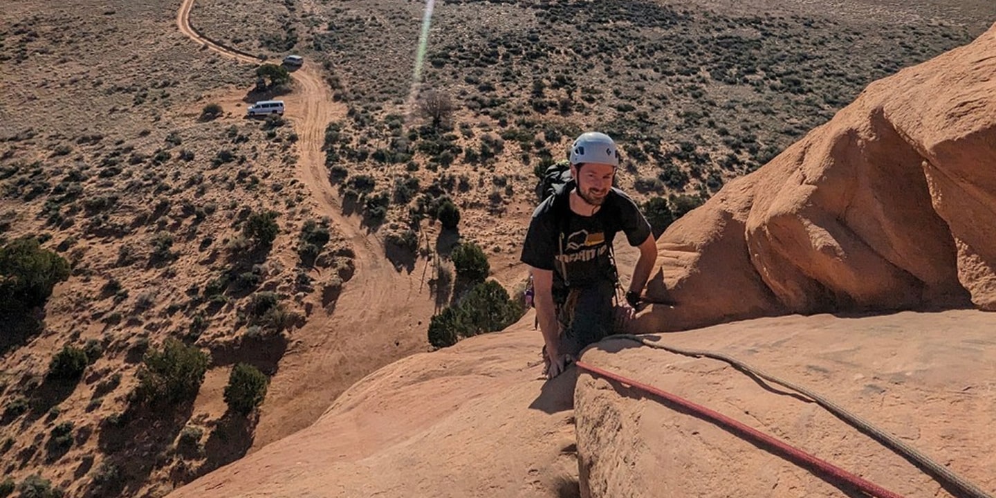 A rock climber at the top of looking glass arch in moab