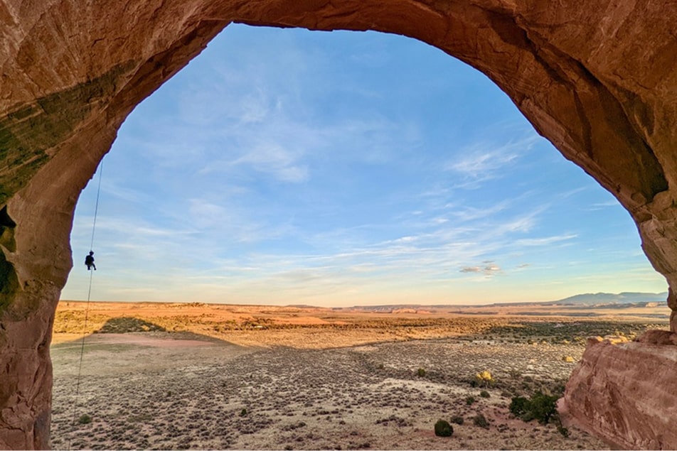 A person rappels down looking glass arch in Moab