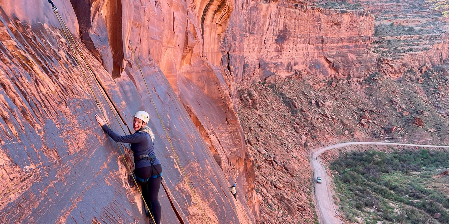 A woman rock climbing on red rock above a road