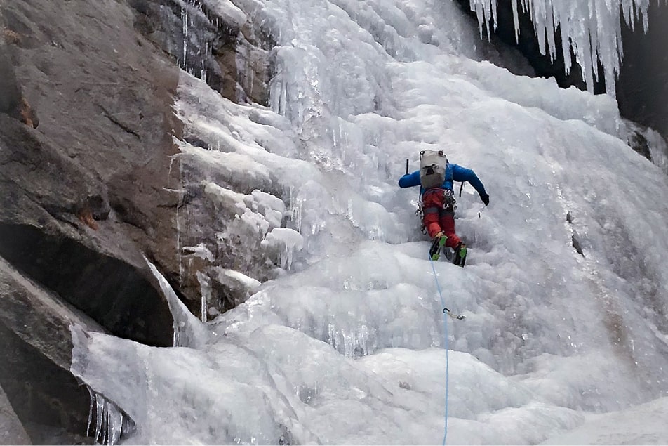 A man ice climbing is halfway up a waterfall
