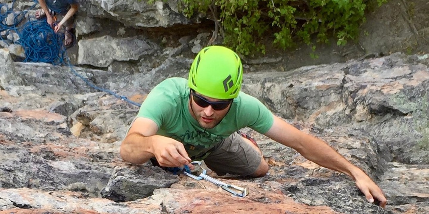 A man learning to lead climb places his quick draw