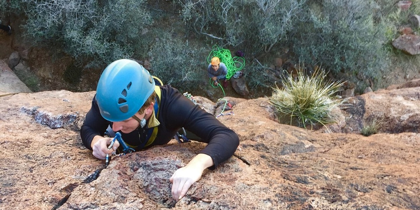 A woman learning to lead climb places her climbing equipment