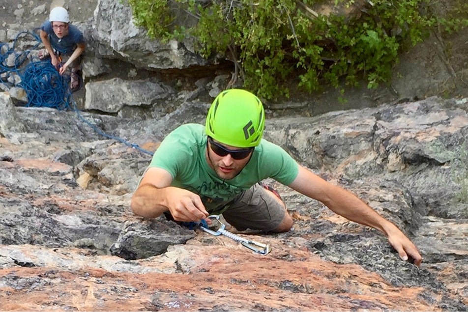 A man learning to lead climb places his climbing equipment