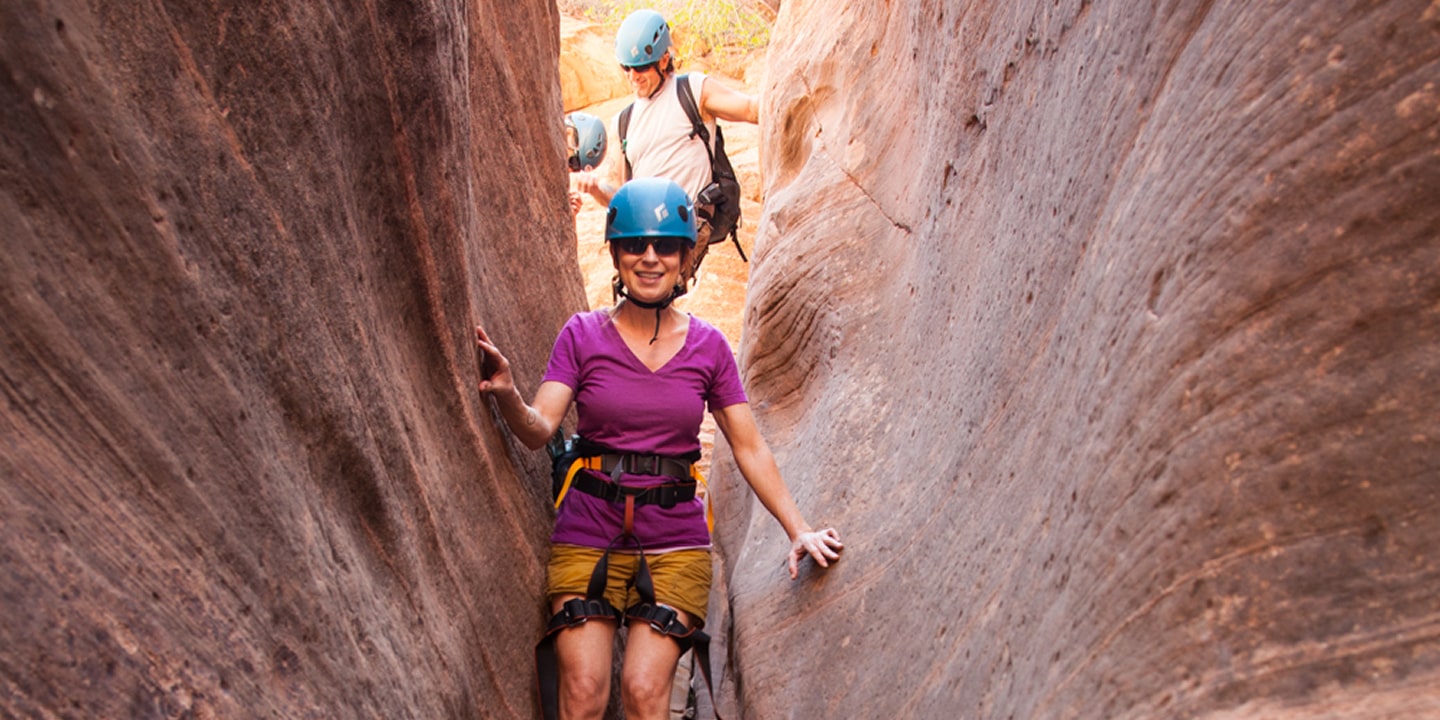 A woman in a purple shirt walks through a narrow slot canyon