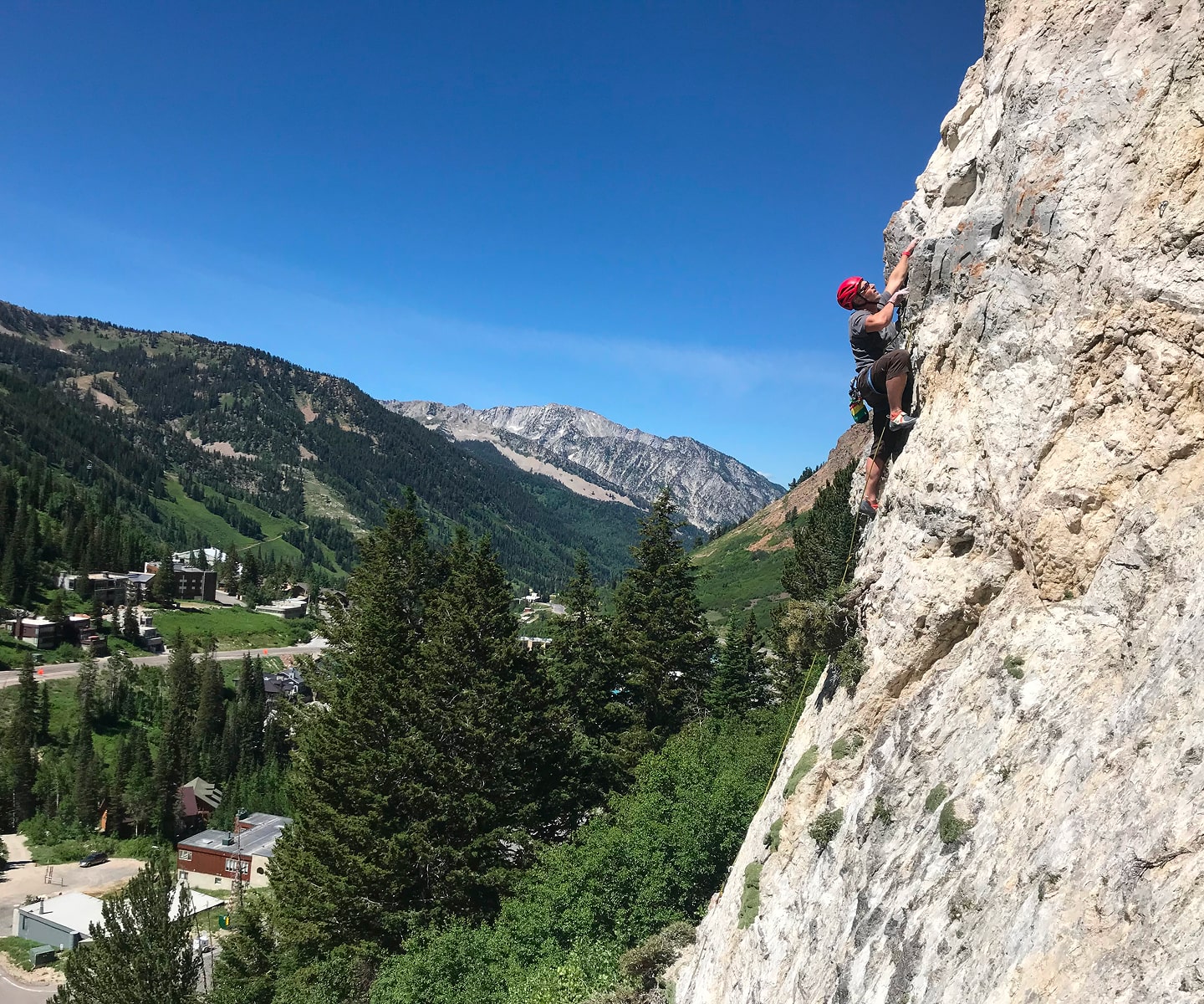 man in red helmet rock climbs with city in the distance