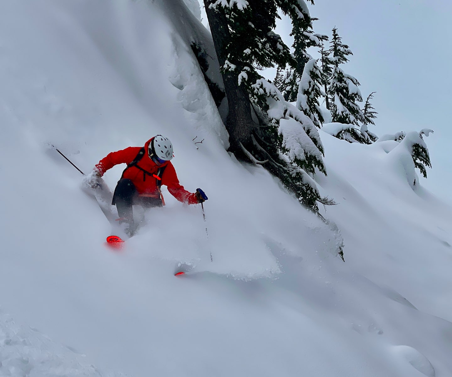man in red jacket slashes deep powder on steep terrain