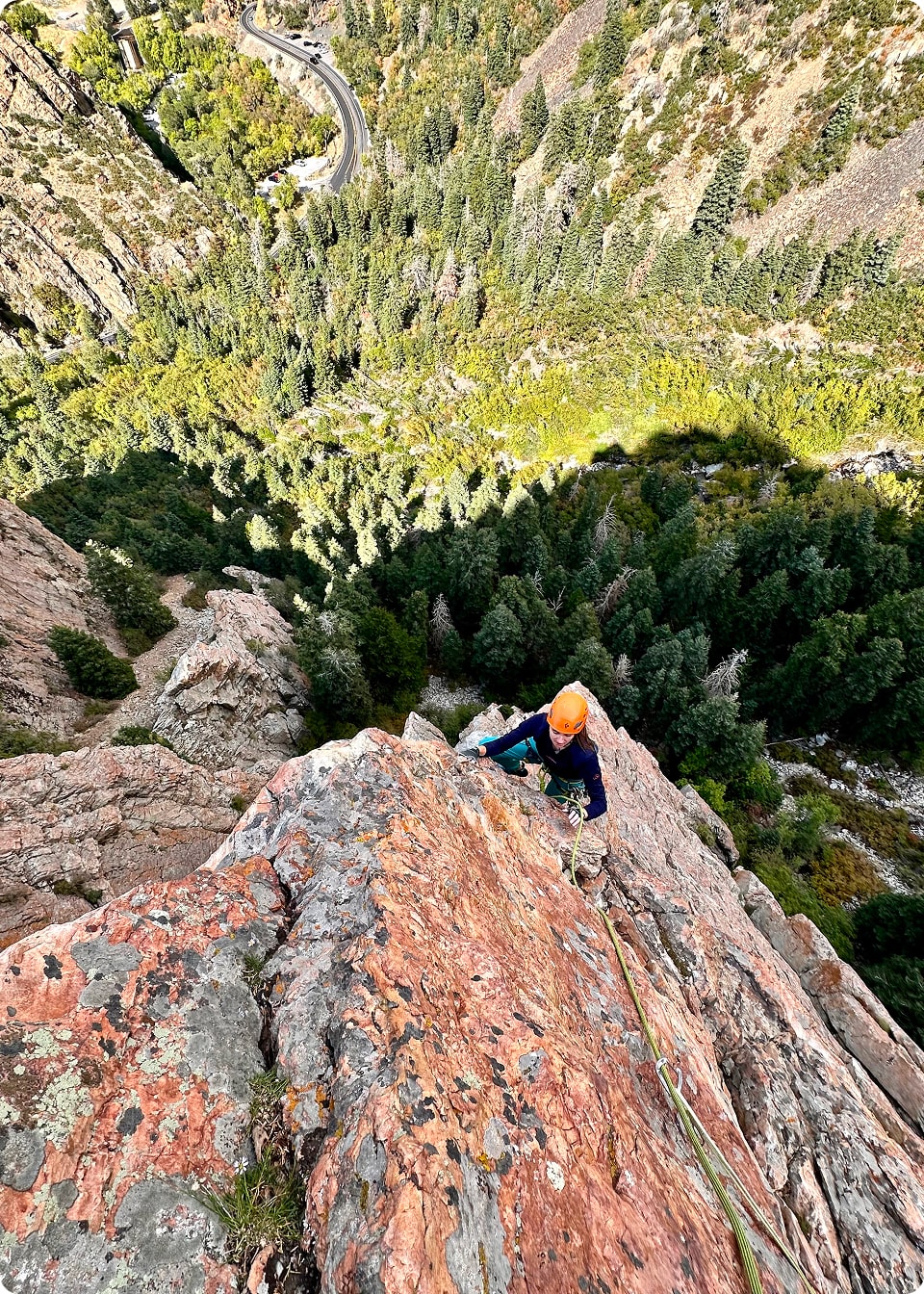 A person in an orange helmet climbs a large rock