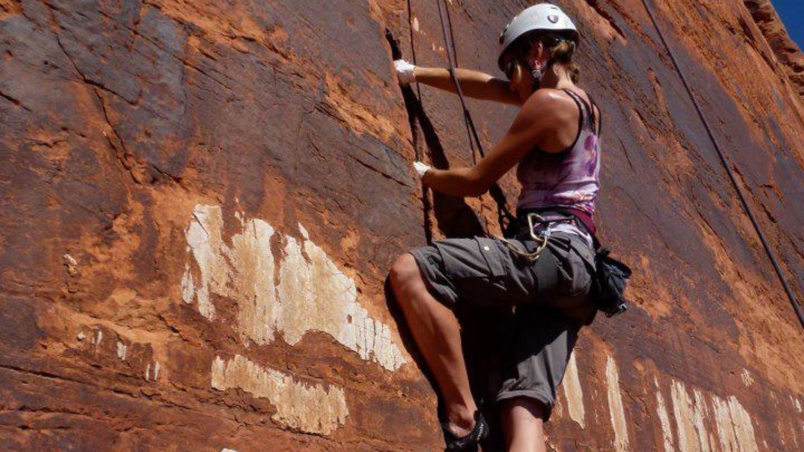 a woman climbs a cracked rock formation in Moab