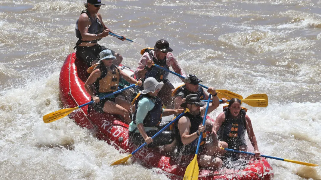 A red raft filled with people with paddles navigates white water
