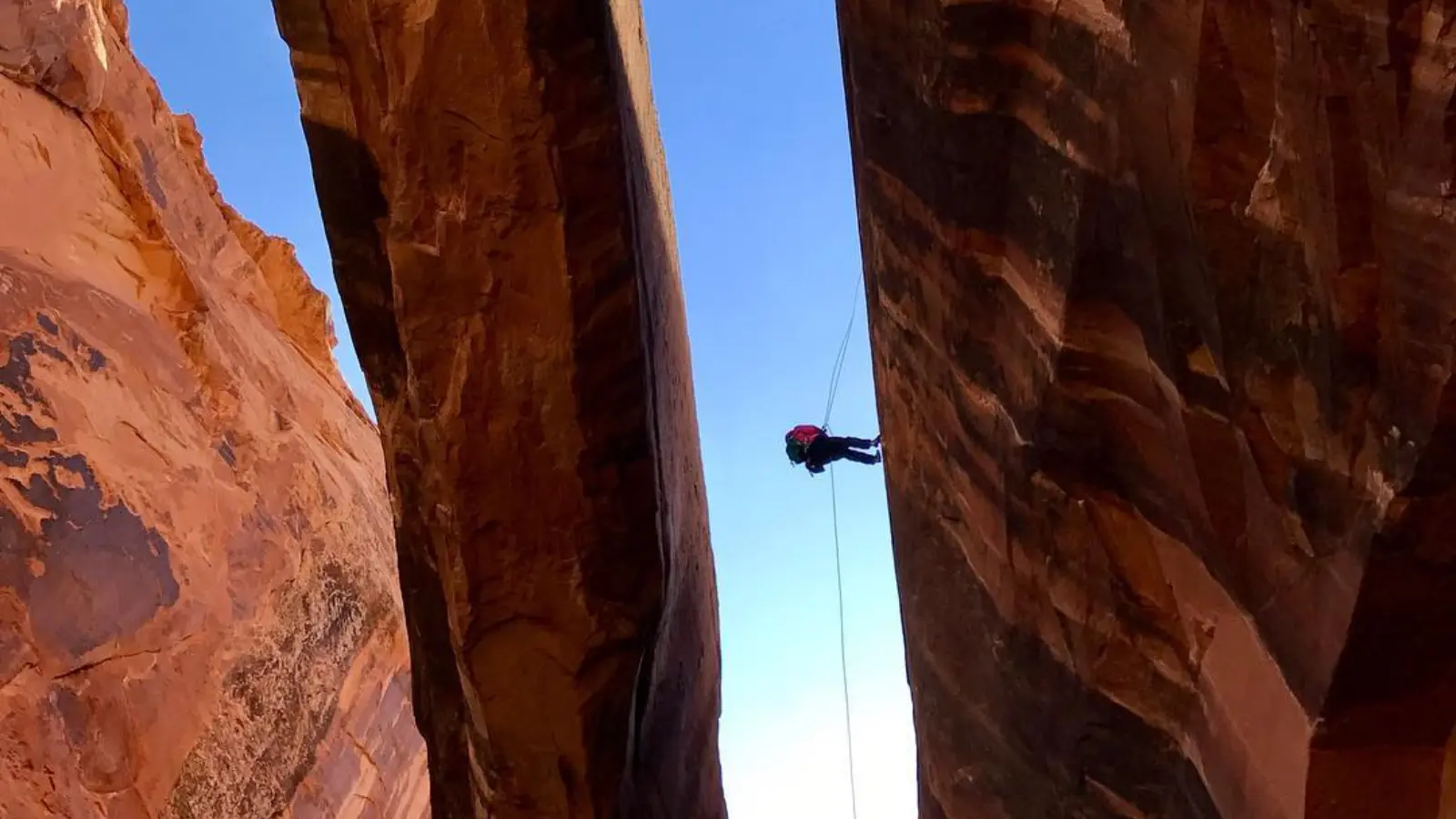 A person rapells through a large arch in Moab
