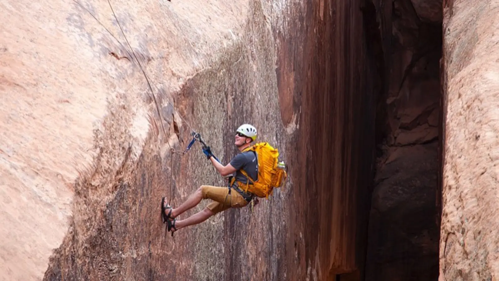 A man canyoneers down a rock wall in a yellow backapck
