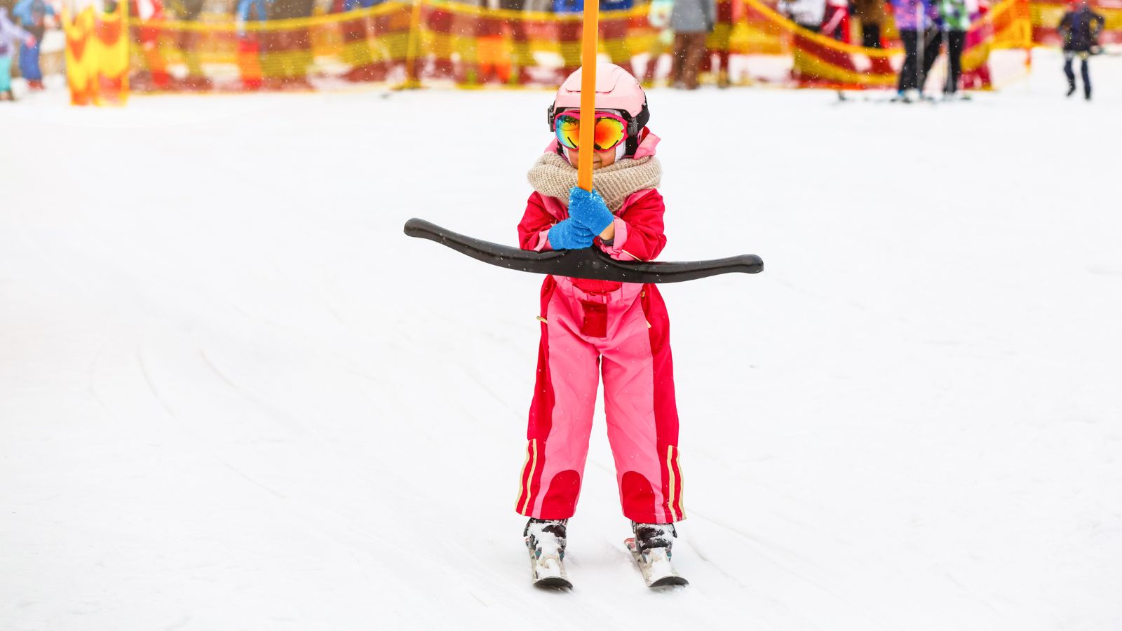 A girl in a pink ski suit holds onto a T bar at a ski resort