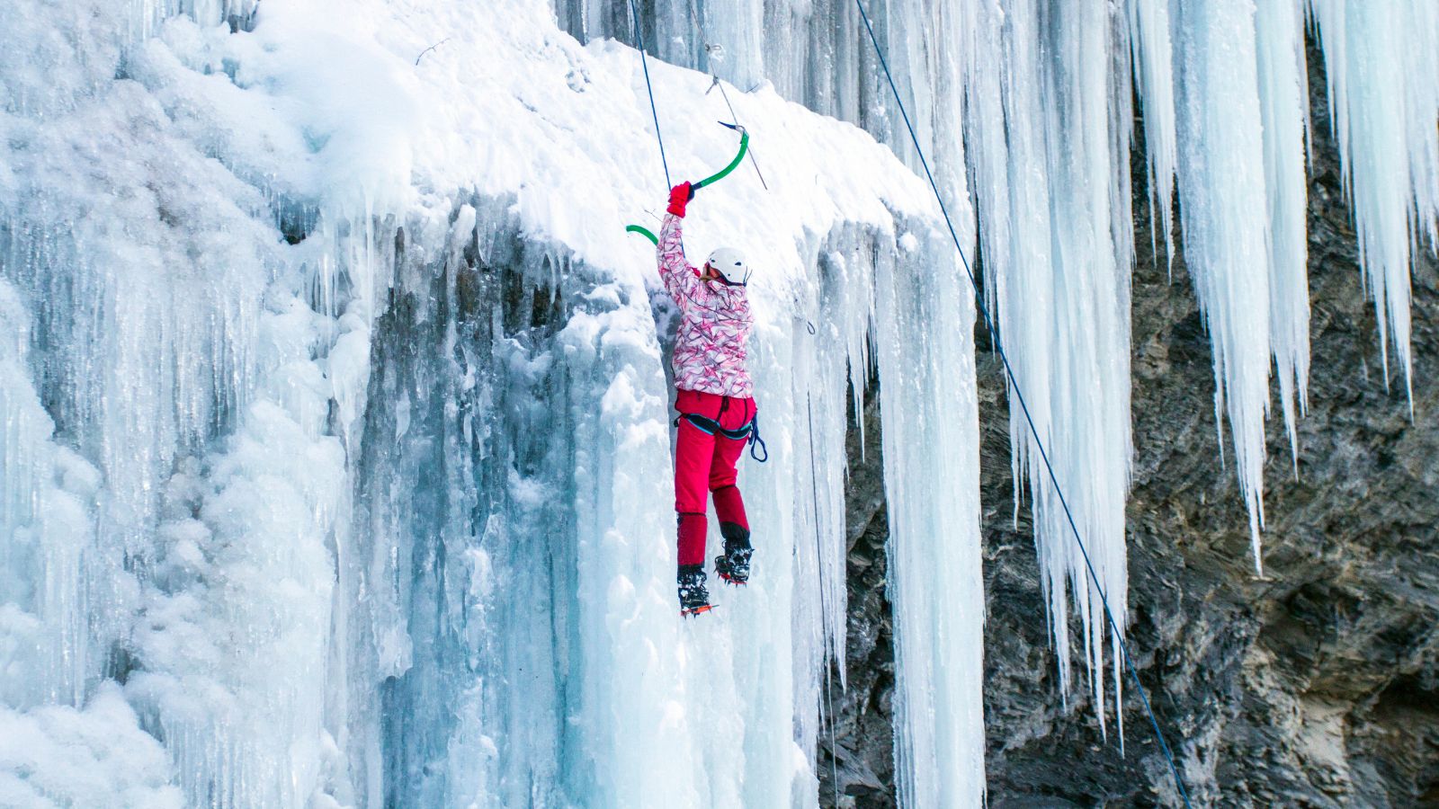 A person in pink ice climbing with a green ice axe