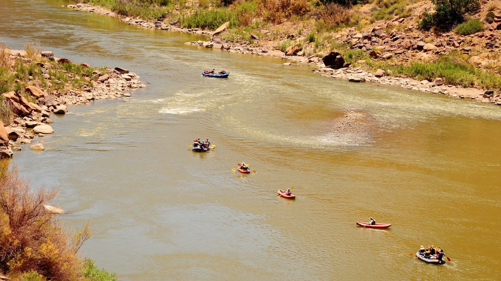 A group of rafts a kayaks float the river in moab